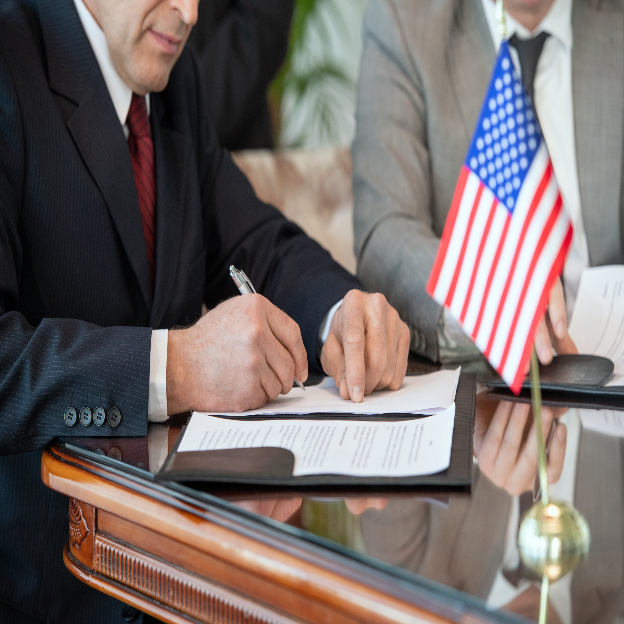 Executives signing official papers beside a U.S. flag, illustrating traditional document workflows transitioning to Electronic Signatures and electronic contract signing.