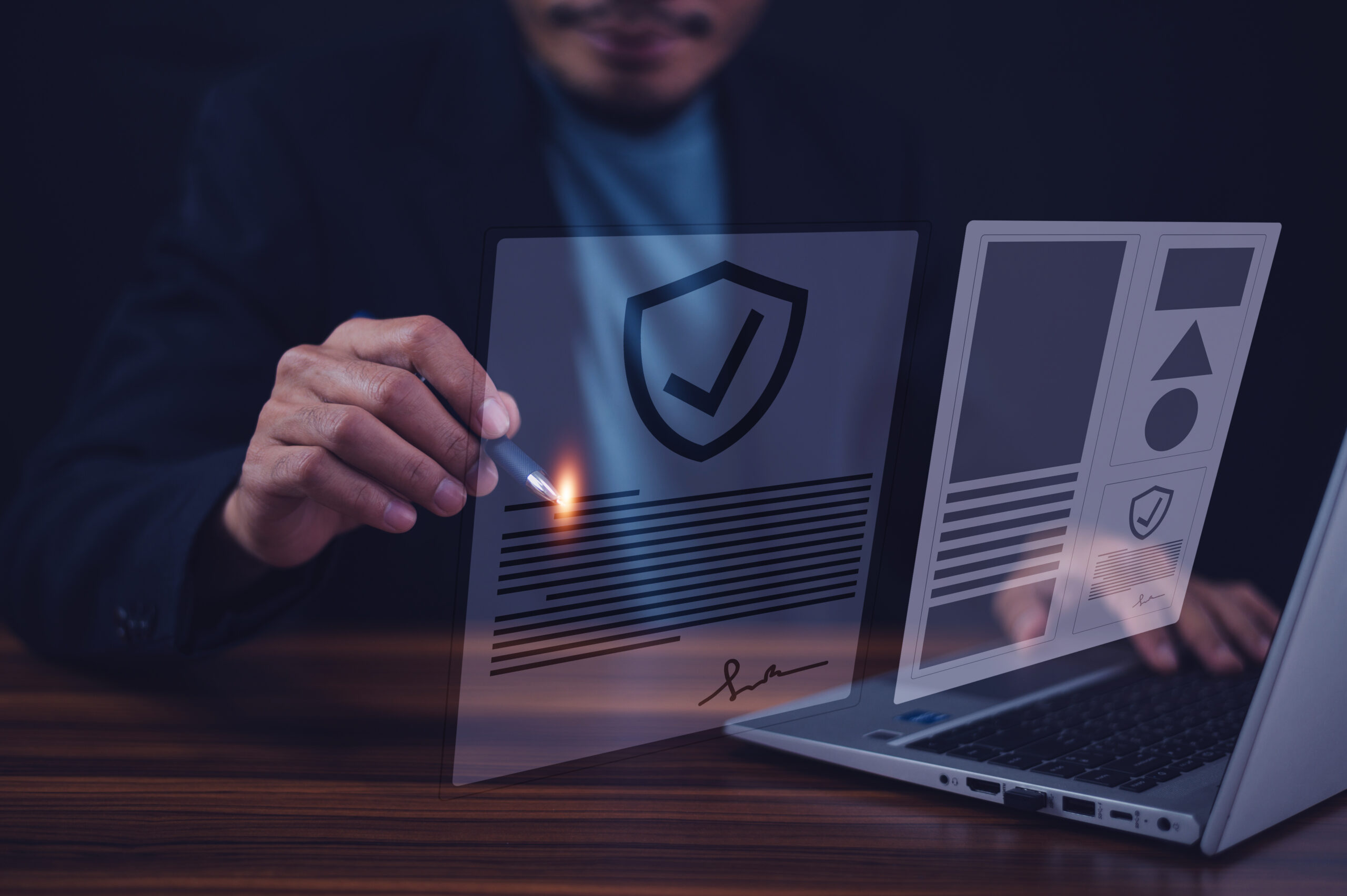 Person holding a pen with light beam pointing at transparent digital documents displaying security shield icons with checkmarks, working on a laptop in a dark setting, representing digital document security and verification