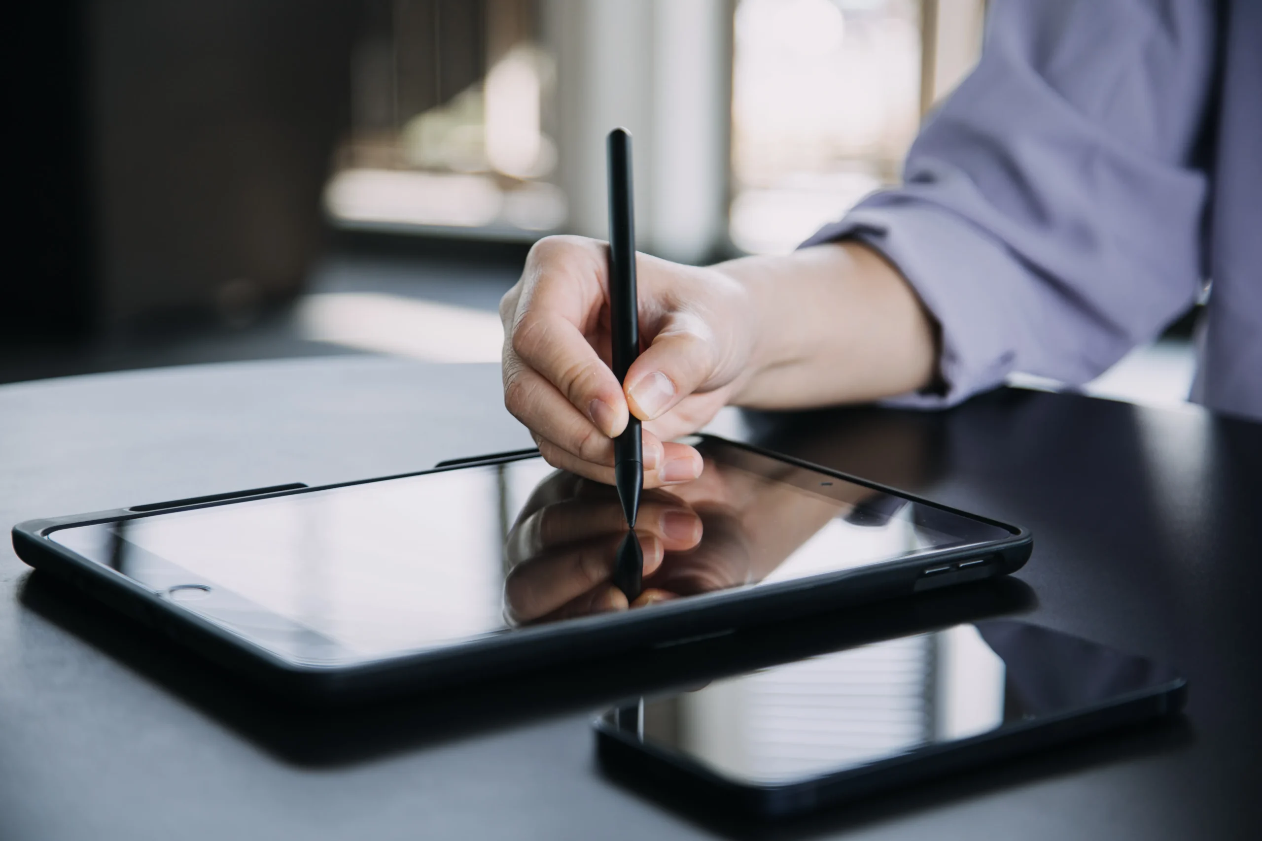Professional using digital pen on graphics tablet next to laptop on wooden desk for digital design or e-signature work