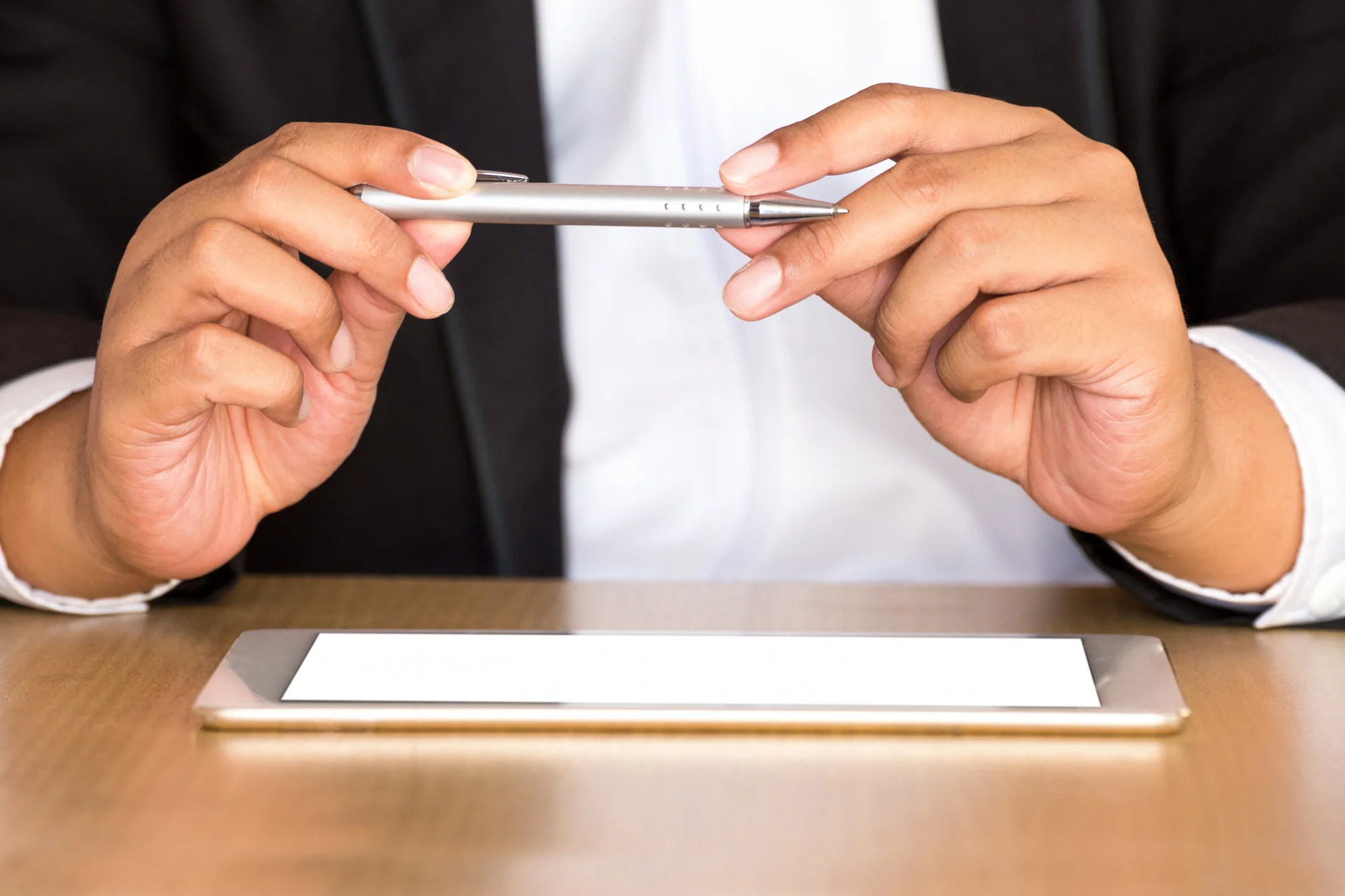 Business professional in suit holding silver stylus pen with both hands above digital tablet on desk