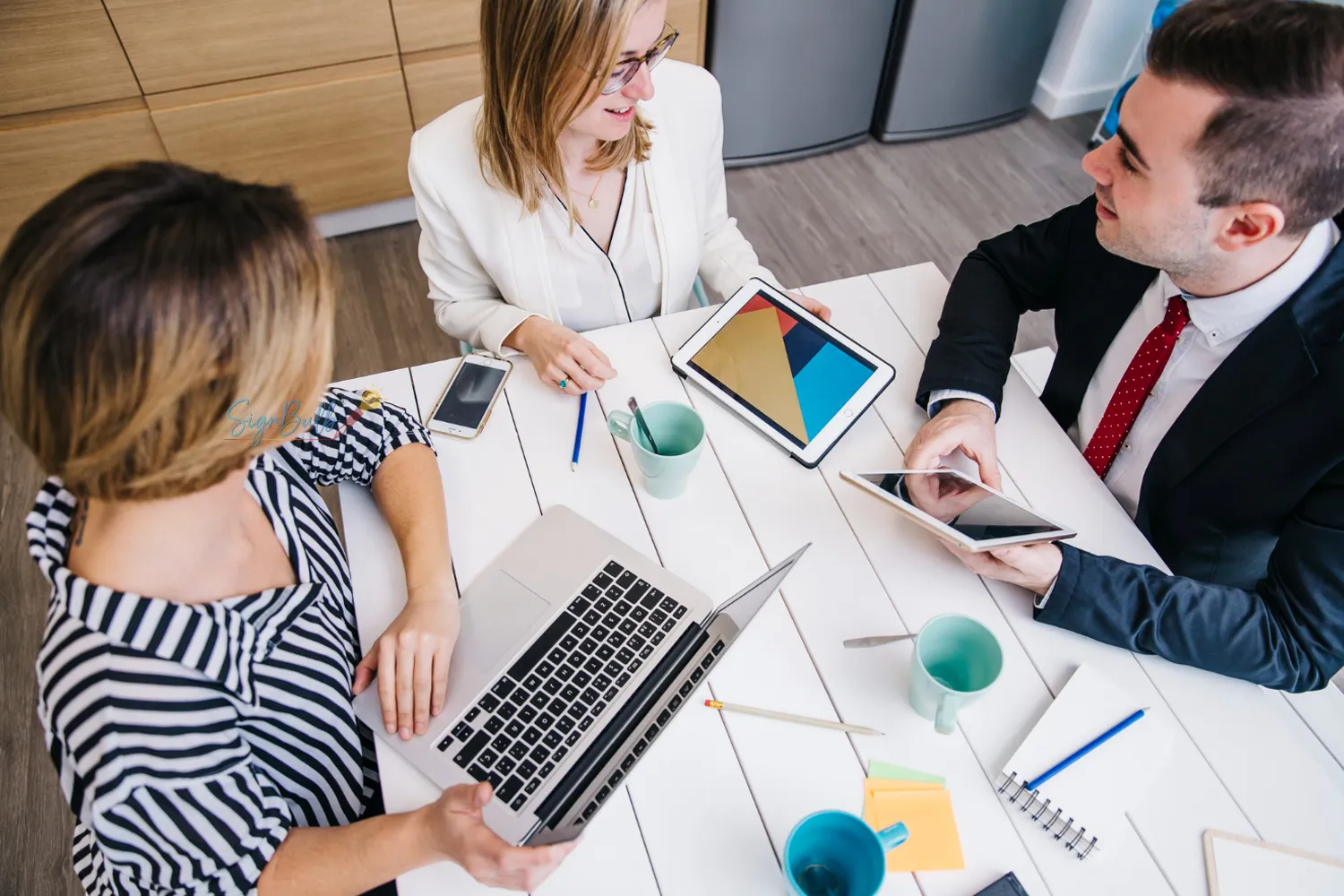 Business professionals collaborating at a table using tablet and laptop for secure digital agreements and eSignature workflow management