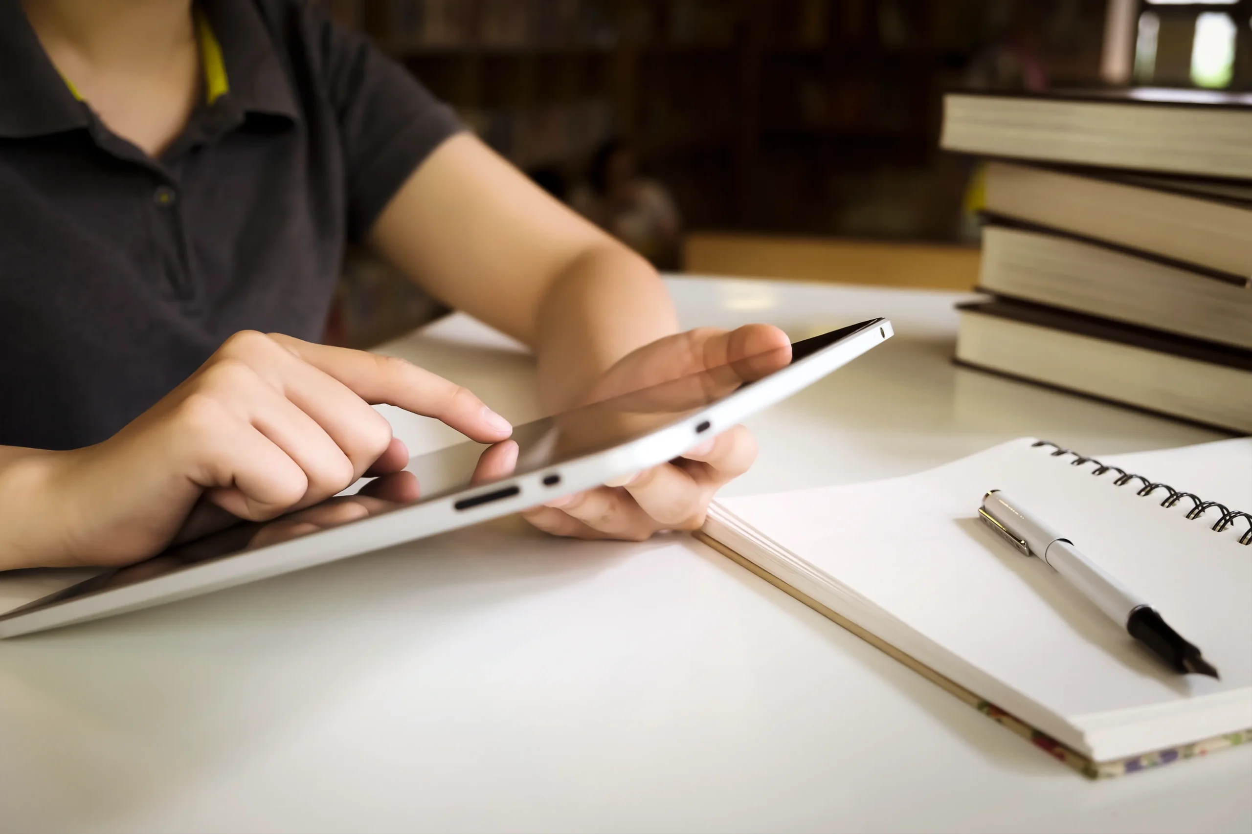 Student completing a student enrollment form signature online using a tablet next to textbooks.