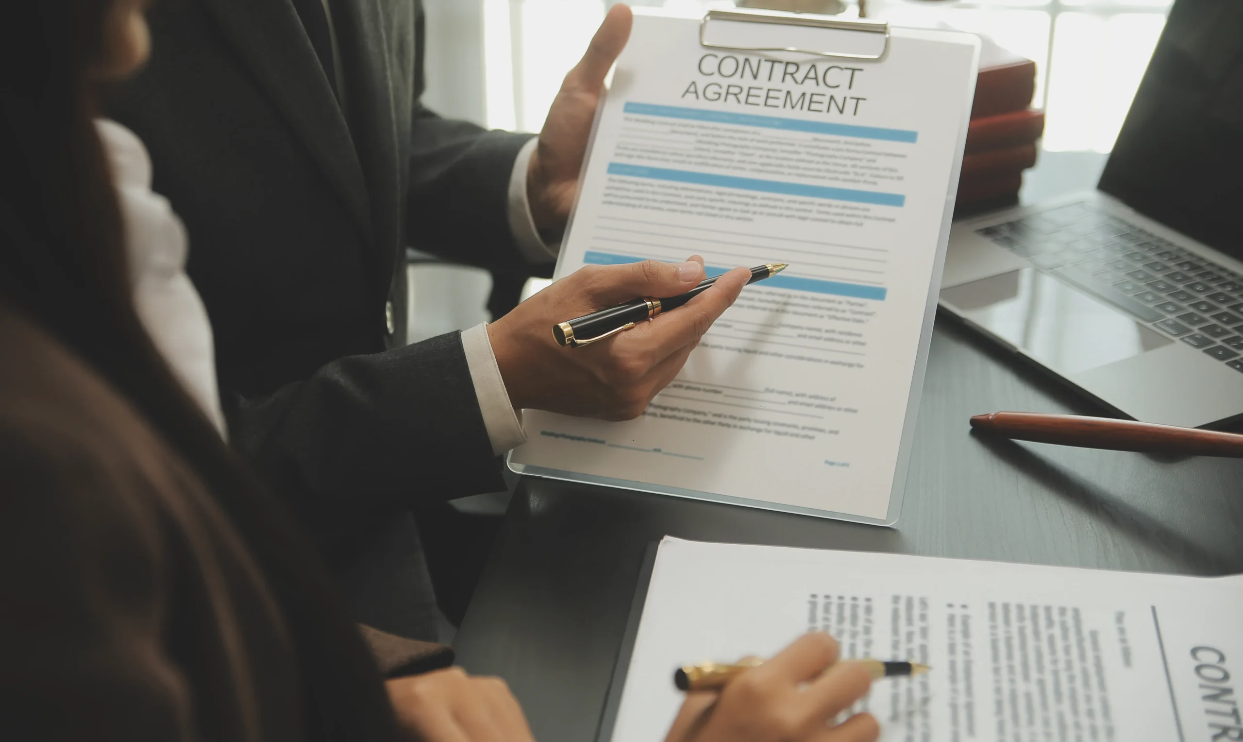 Business partners reviewing a contract agreement form next to a laptop for electronic contract workflow management.