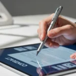 A close-up of a professional signing a digital contract labeled "CONTRACT" on a tablet with a silver stylus, demonstrating how to execute e signature procurement contracts.