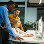 A business team standing around a computer monitor, reviewing analytics integrated with electronic signature software for sales.