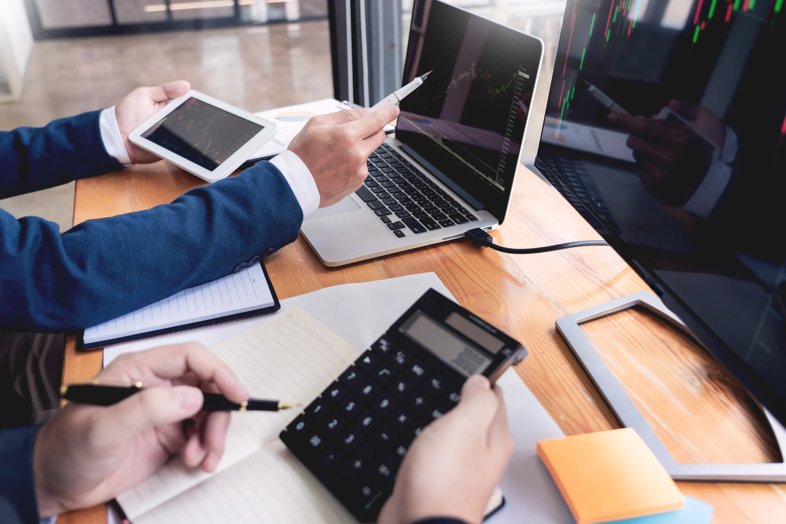 A business team analyzing financial growth charts on multiple screens and calculators, showcasing how an easy signing app can help cut corporate costs and reduce signature drag.