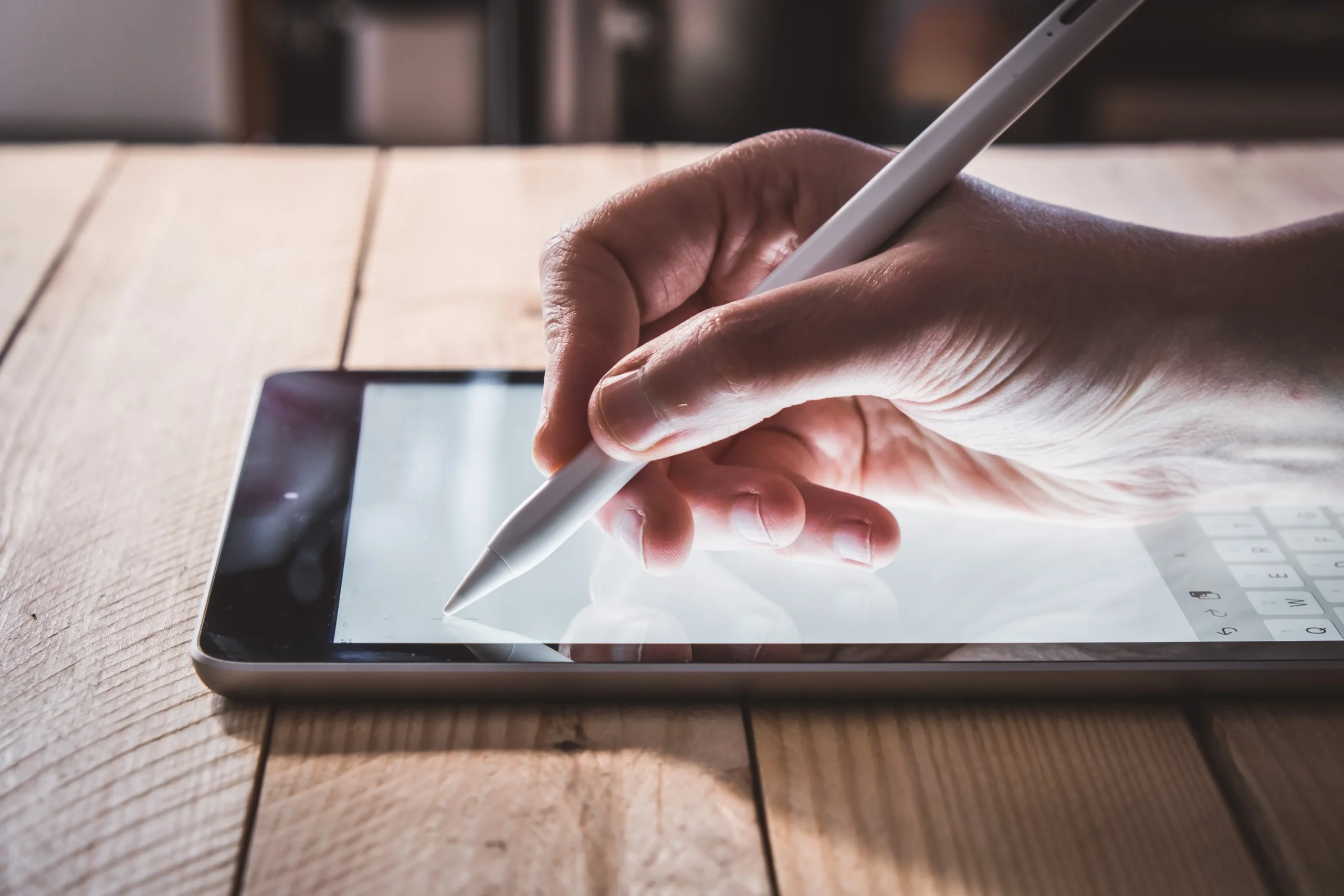 A close-up of a person's hand using a stylus pen to sign a document on a tablet screen, highlighting a practical comparison of HelloSign vs Signbulb.