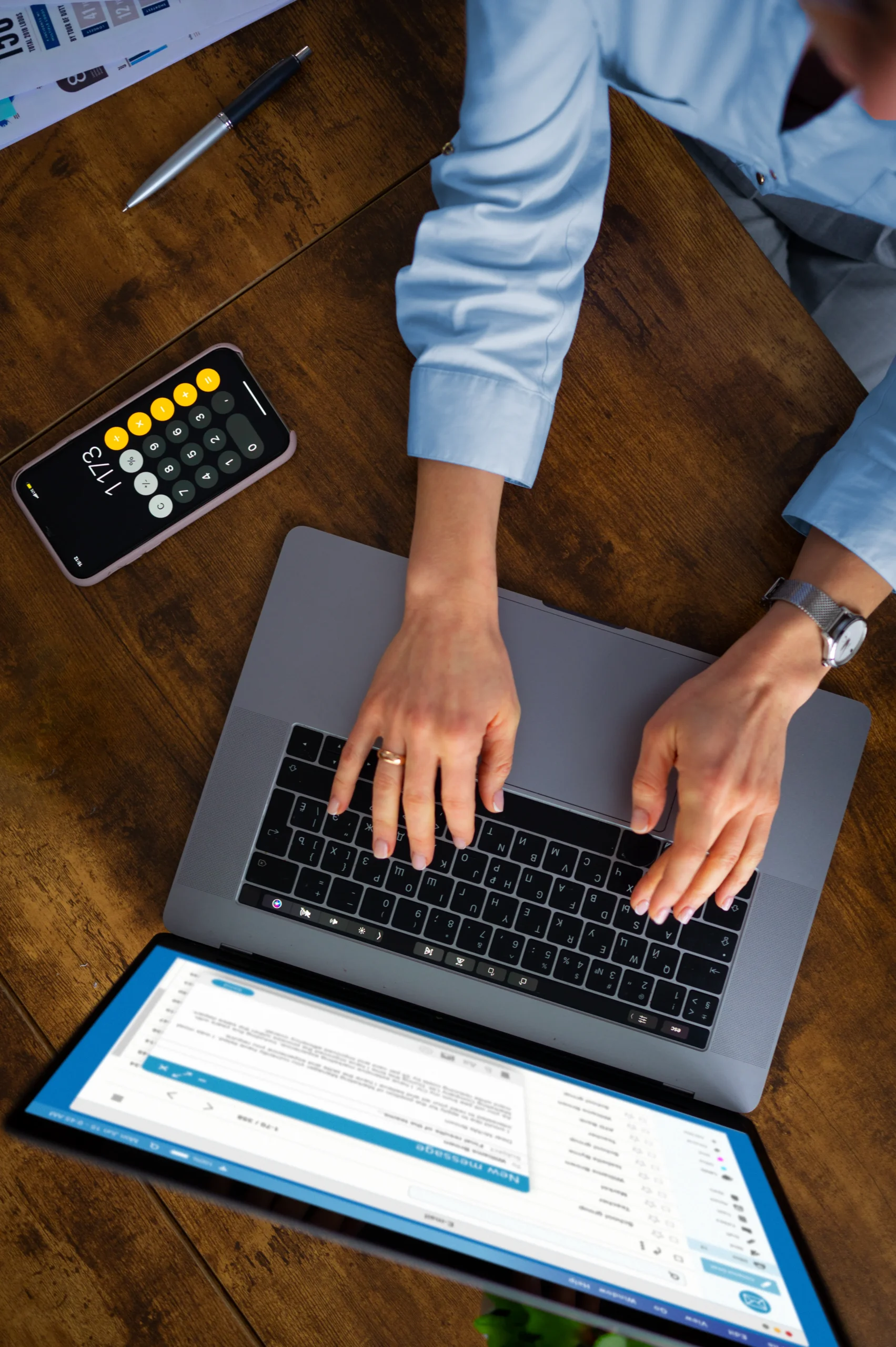 An overhead view of a businesswoman typing on her laptop at a wooden desk with a phone calculator nearby, highlighting the return on investment of modern digital document signing.