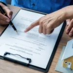 Real estate agent pointing at the signature line on a document next to a house model, demonstrating real estate electronic signatures.