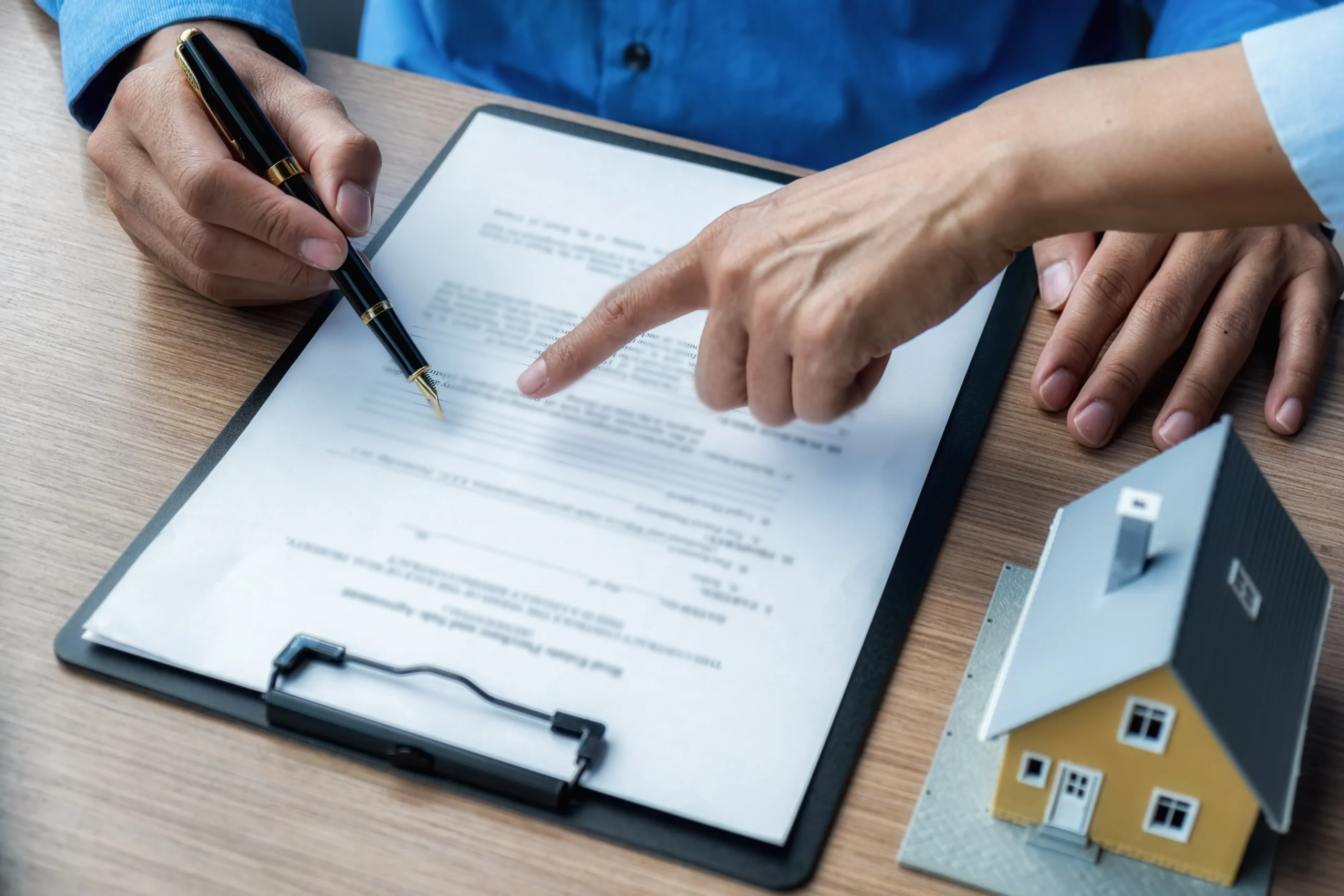 Real estate agent pointing at the signature line on a document next to a house model, demonstrating real estate electronic signatures.