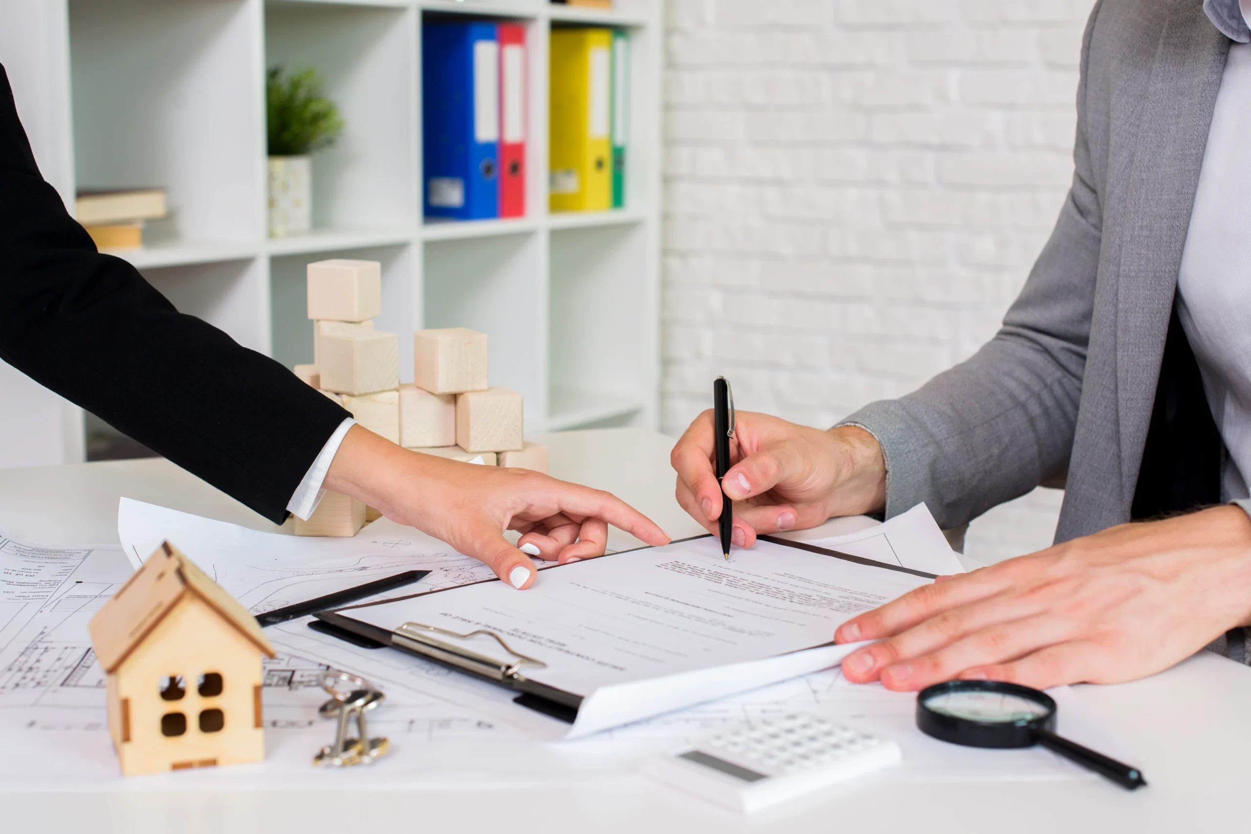 A client signing paper paperwork for real estate document signing next to a small house model.