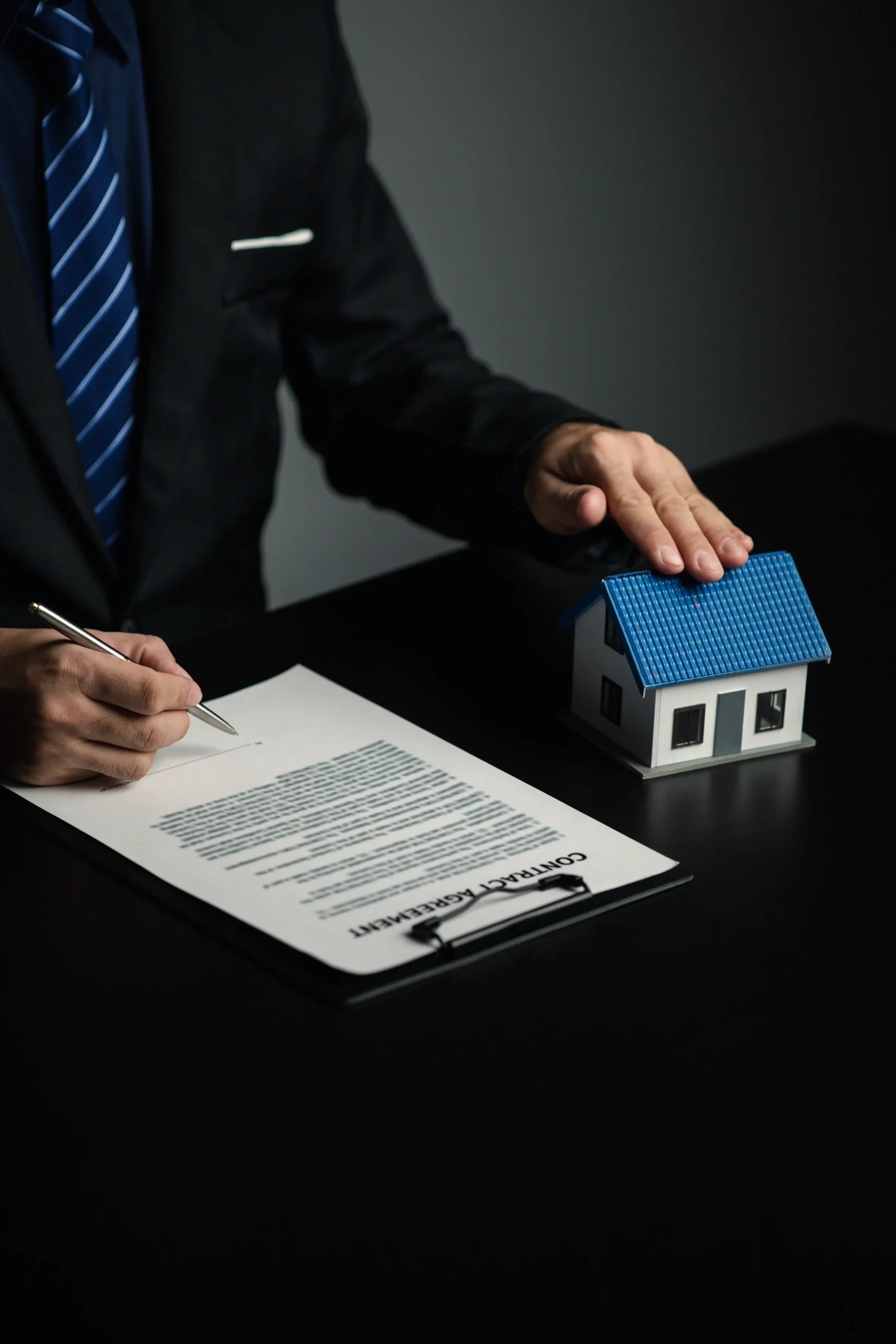 Real estate professional resting his hand on a house model while managing electronic real estate contracts.