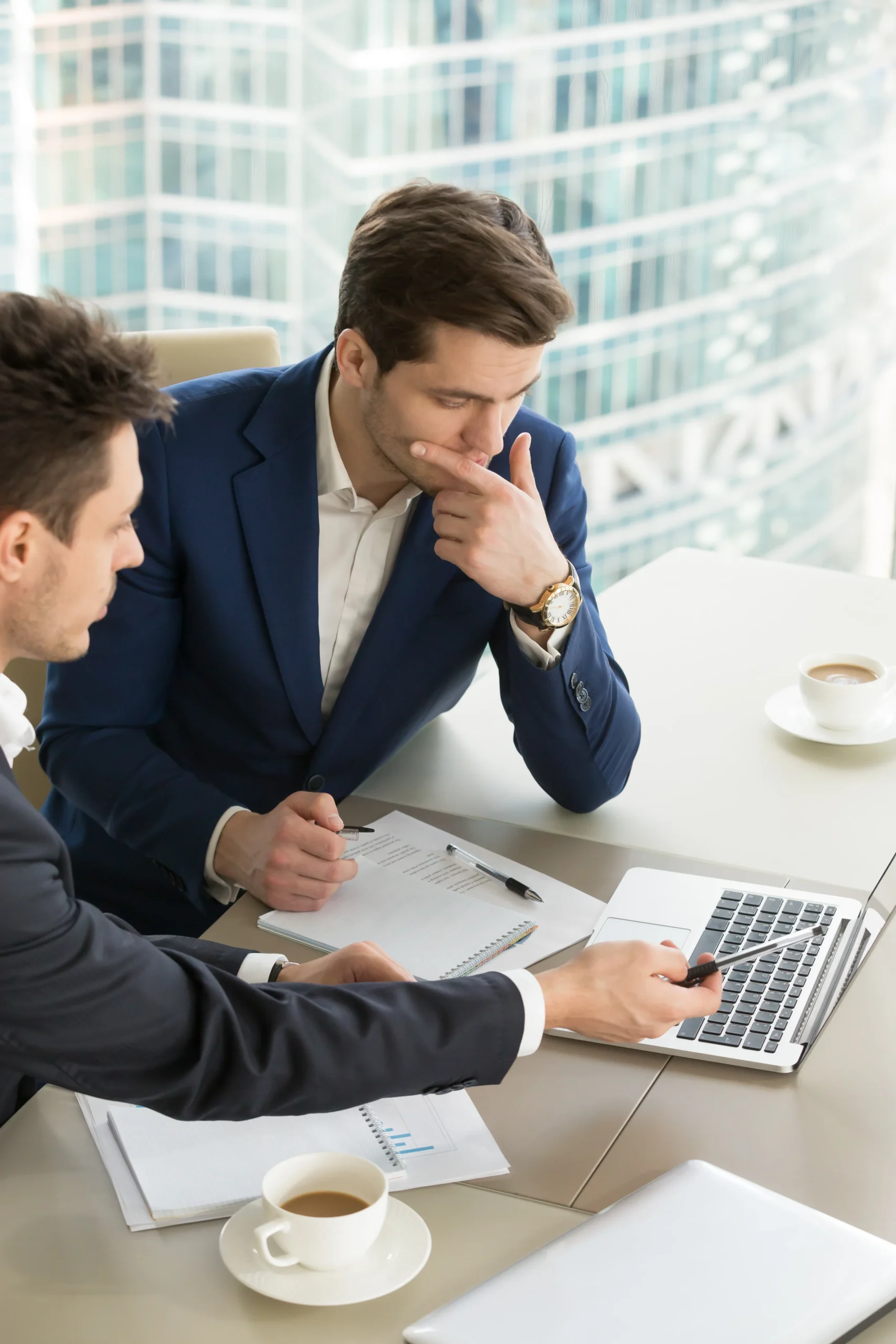 Two businessmen discussing paper contracts and laptop documents to select eSignature software for growing businesses.