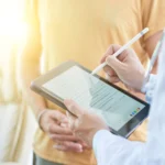 Healthcare provider guiding a patient through completing a patient consent form online using a digital tablet.
